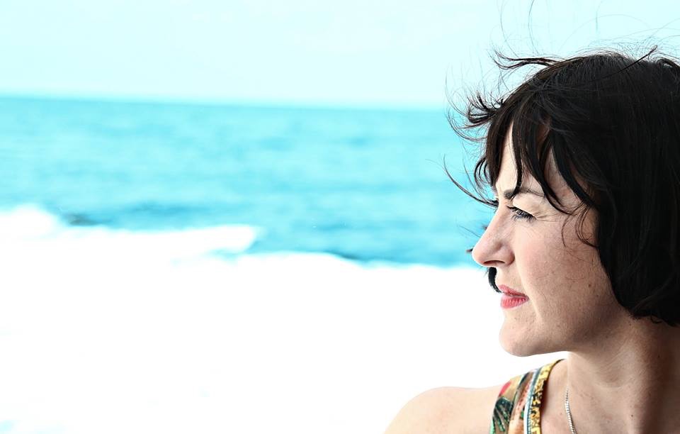 20141107_052656000_iOS Wind-blown profile view of Caroline standing before light blue ocean water