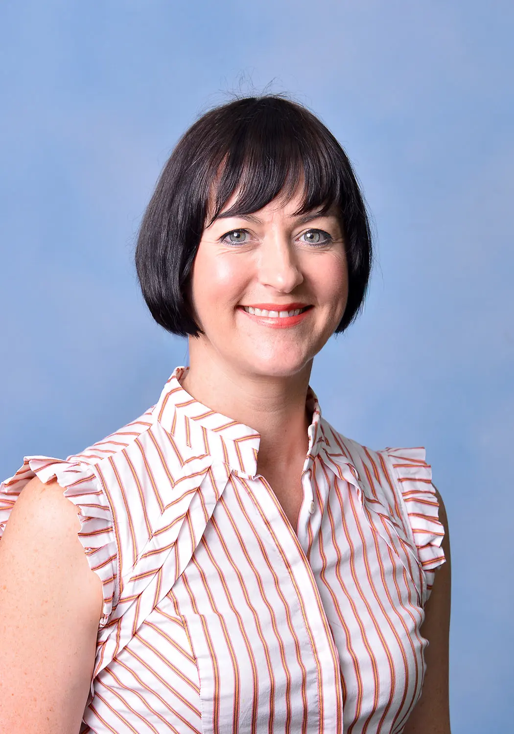 Caroline smiling warmly in a portrait set against a blue background